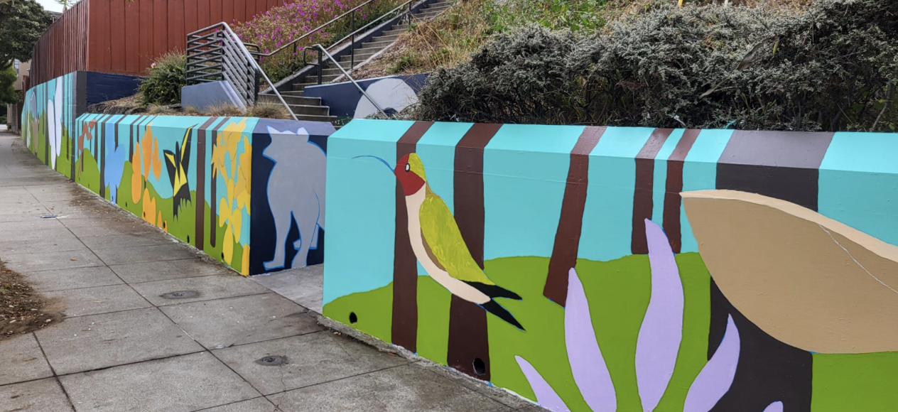 Mural painted on retaining well. Blue background with local birds, flowers, and animals featured.